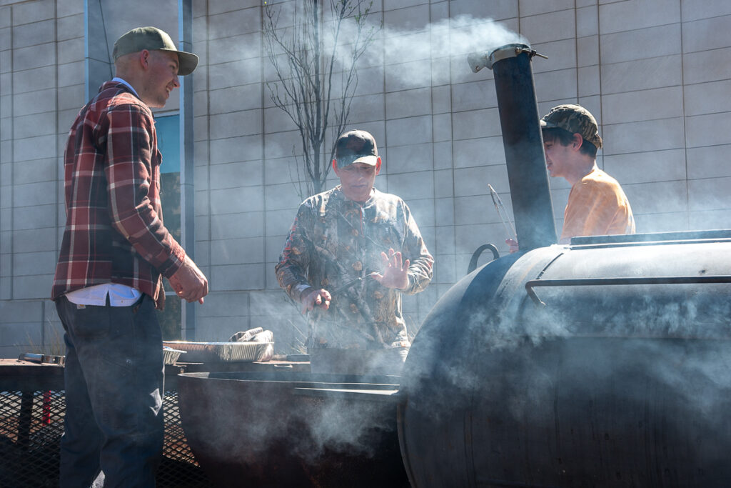 Three people stand beside a smoker outside a building on the UT Institute of Agriculture campus.