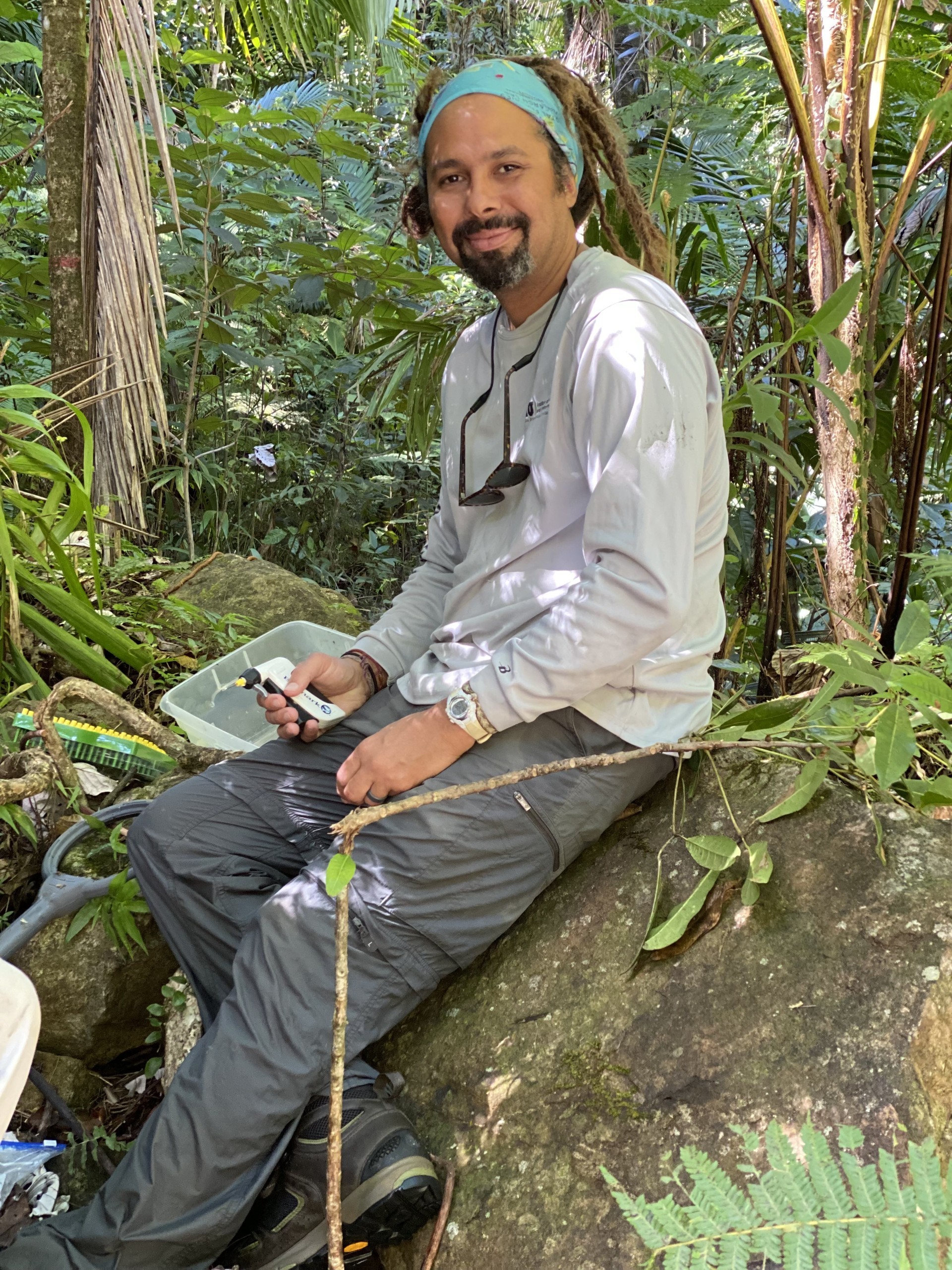 Person sits on rock holding tool in wooded area.