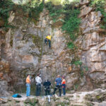 Six people stand below a person climbing a rock at Ijams Nature Center in Knoxville.