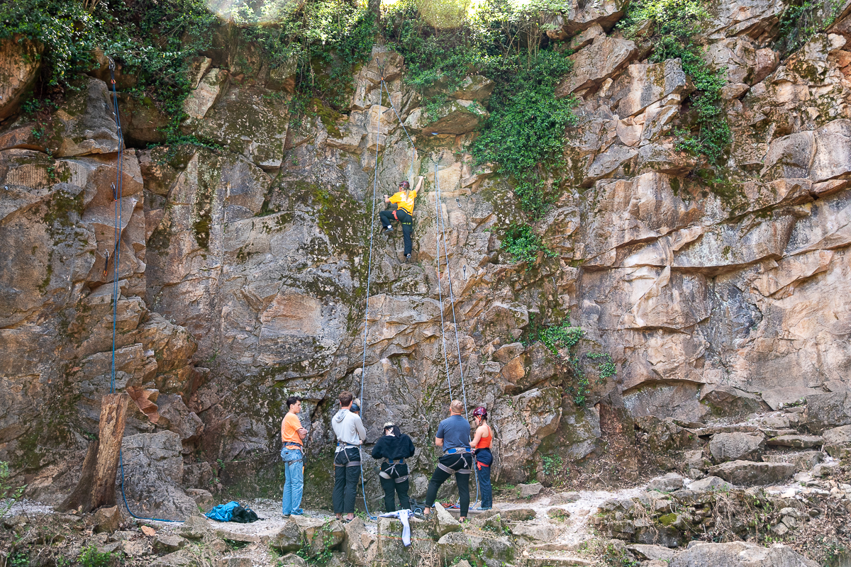 Six people stand below a person climbing a rock at Ijams Nature Center in Knoxville.