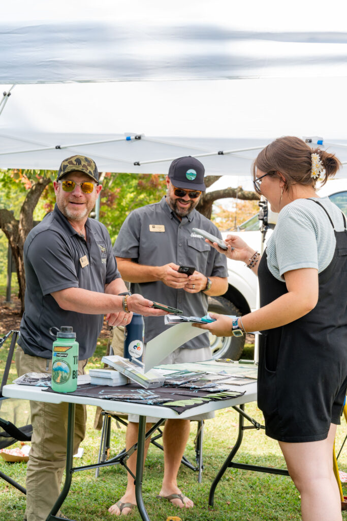 People smile under a tent at a table at the Outdoor Enthusiast Expo.