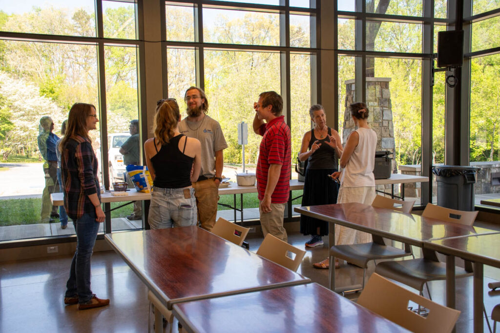 Six people stand inside and two people stand outside the UT Arboretum Auditorium.