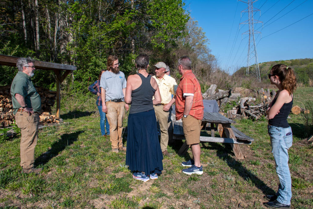 Six people stand and talk at the firewood bank at the UT Arboretum.