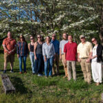 Thirteen people stand and smile in front of a dogwood tree at the UT Arboretum.