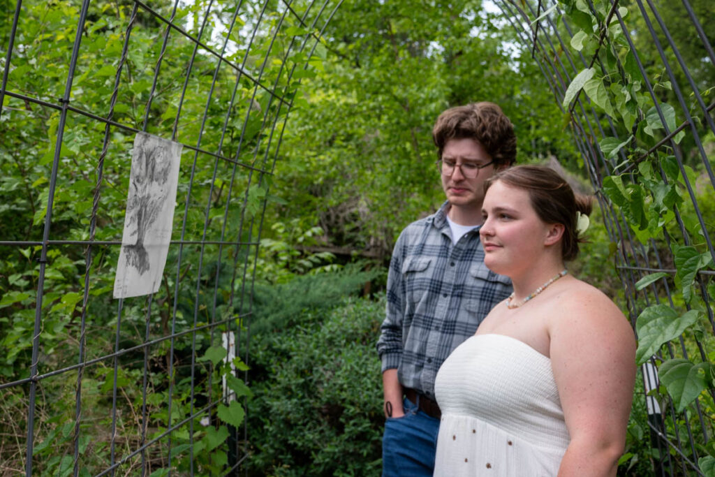 Two people look at a drawing on a wire arch.