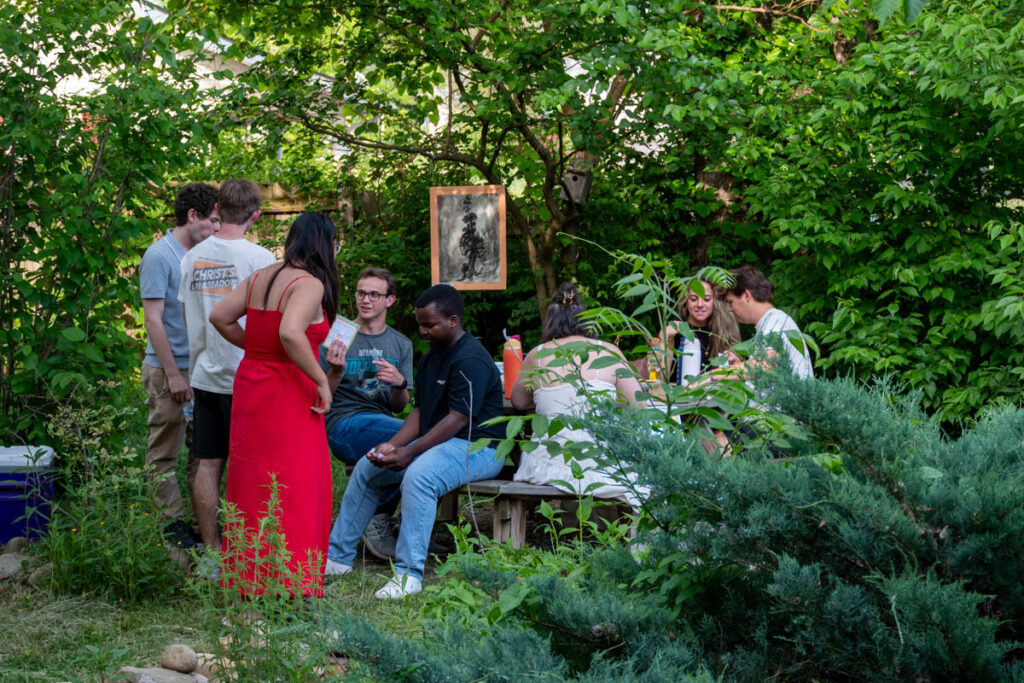 Six people sit around a table and two people stand.