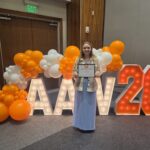 A person holds a certificate in front of a lit up sign and balloons.