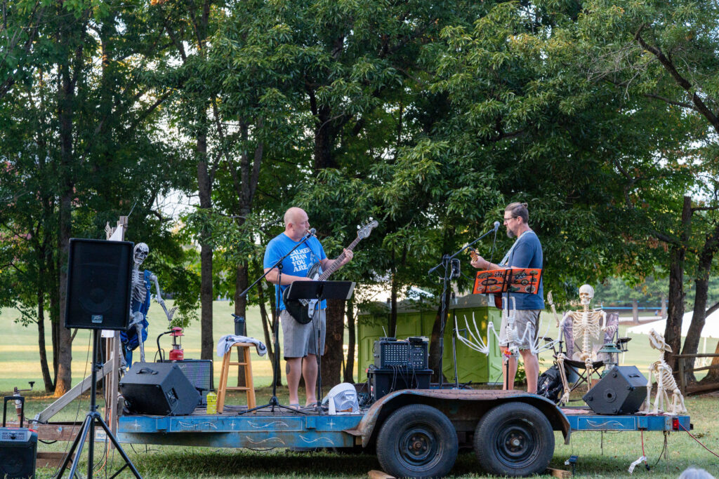 Two people play guitars on a stage with trees in the background on the Maryville College campus.