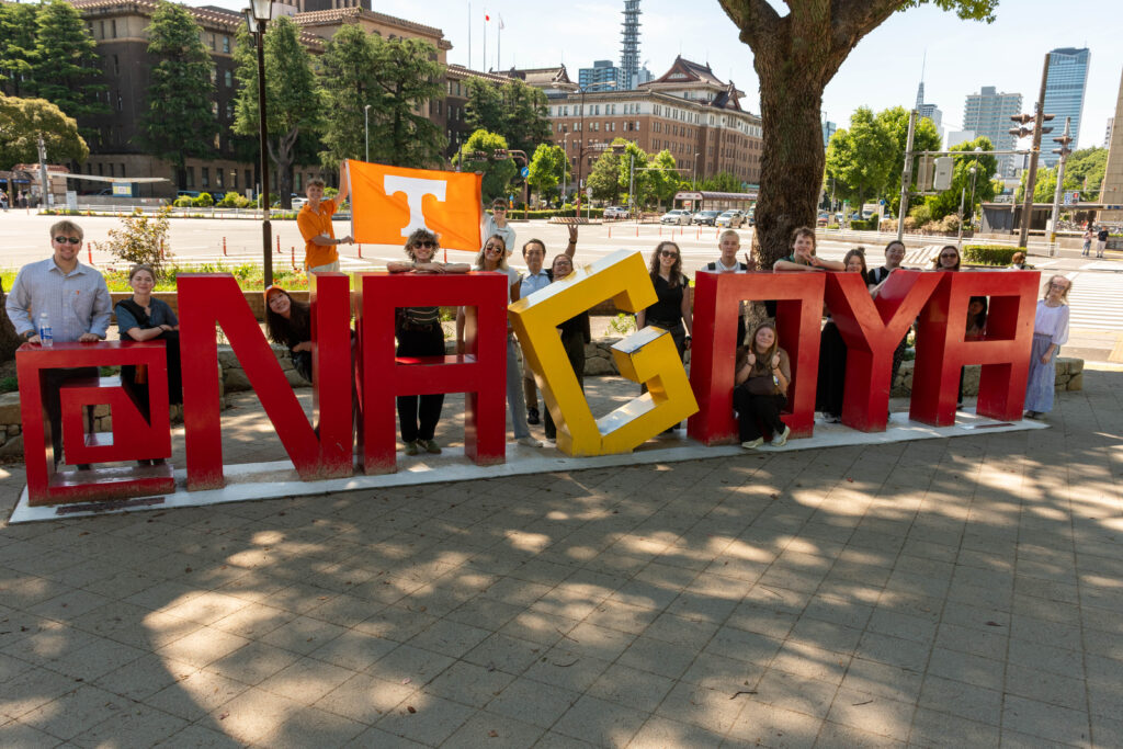 People pose around a sign saying "Nagoya" in Nagoya, Japan.