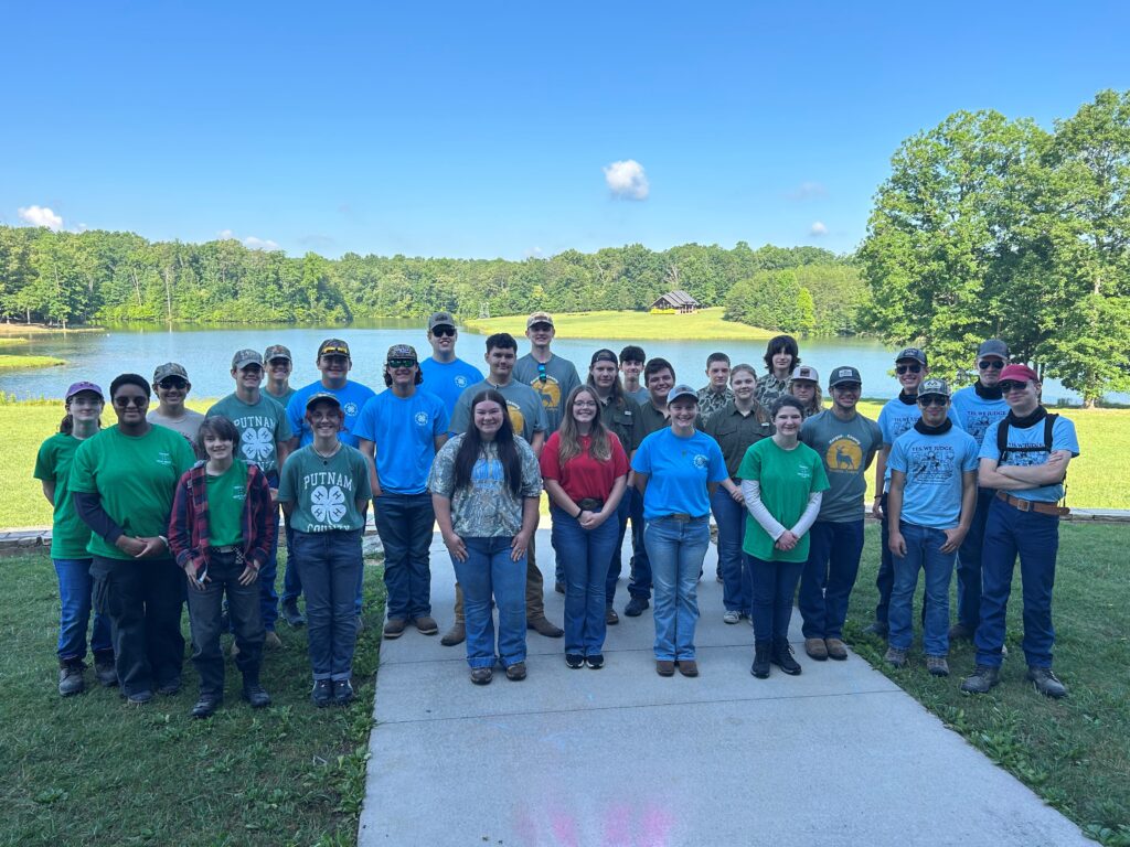 Twenty-eight students stand together in front of a lake.