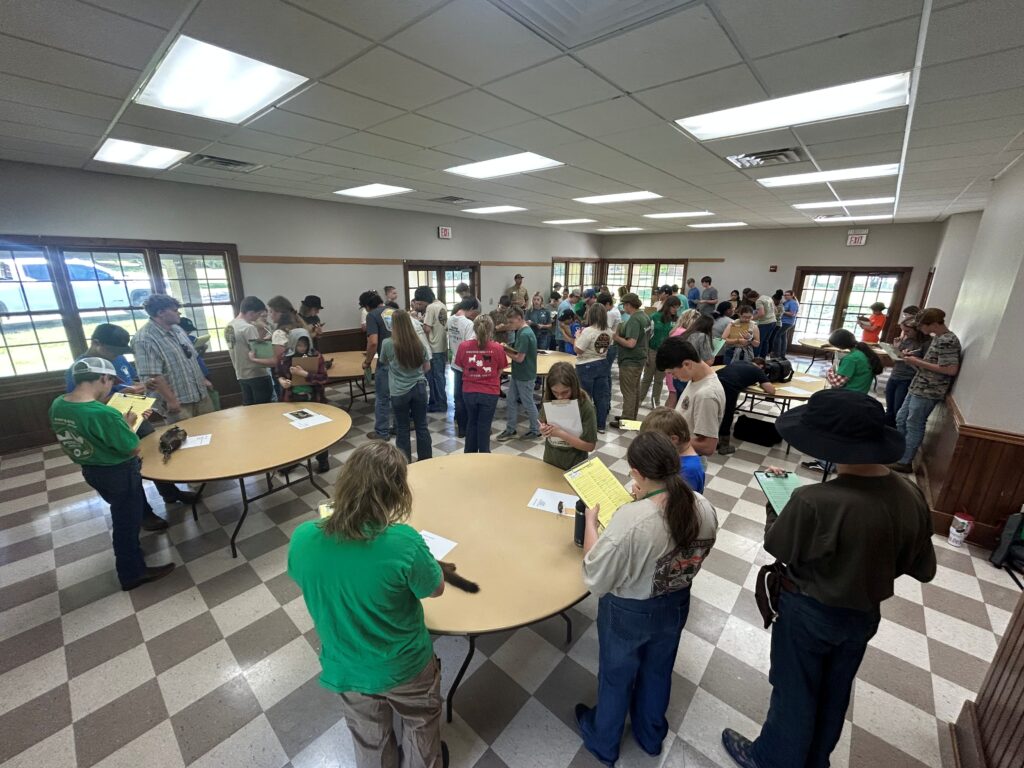 Several students stand around tables with notepads and pencils.