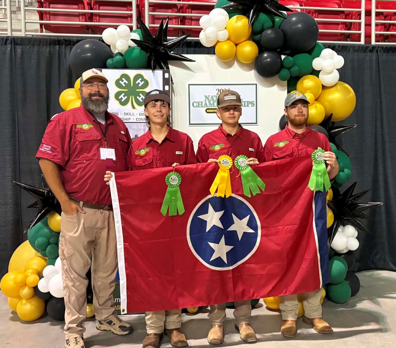 Four people hold the Tennessee flag in front of a 4-H sign with yellow and black balloons.