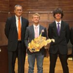 Four people stand on a stage with one person holding a West Virginia-shaped plaque.
