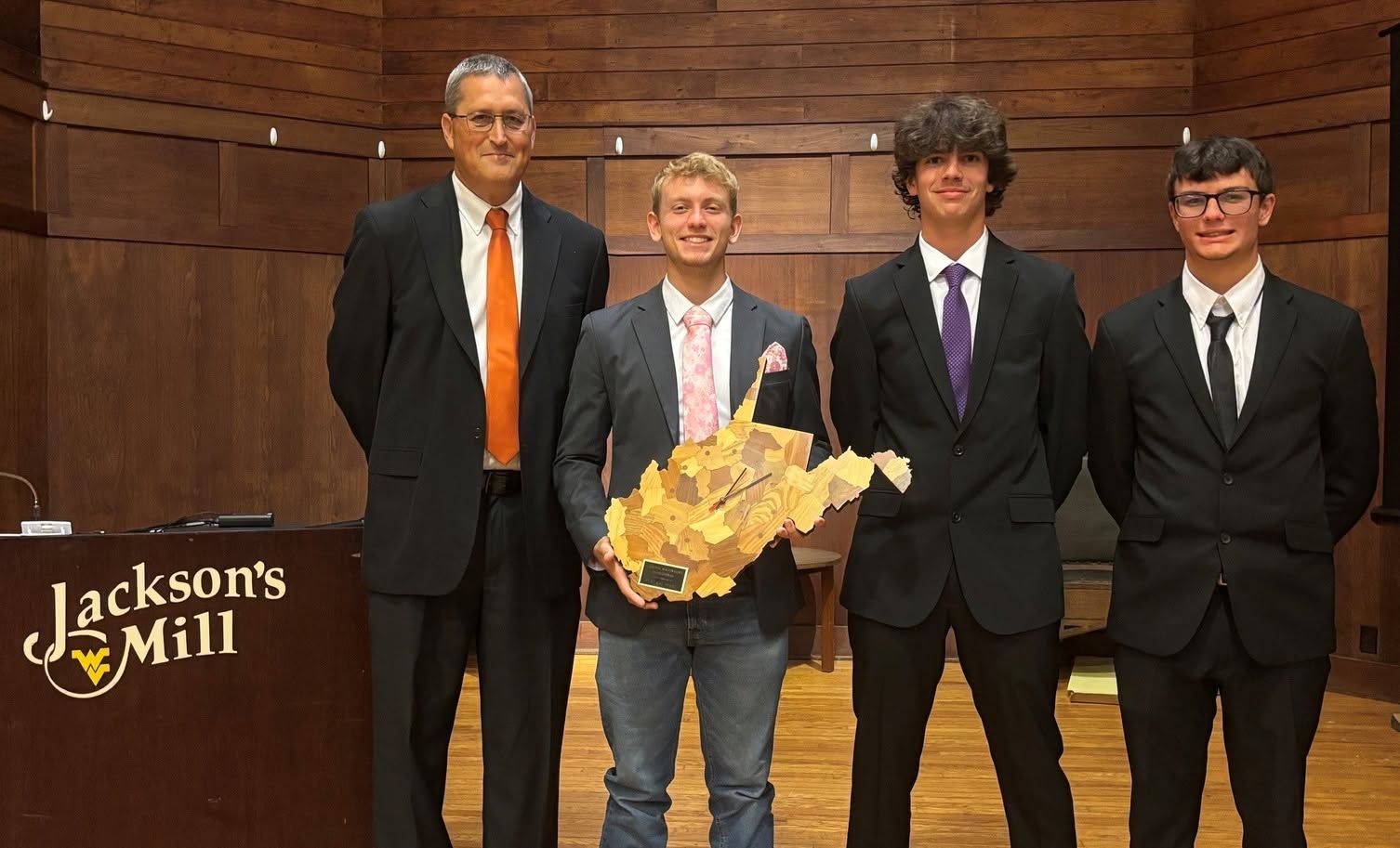 Four people stand on a stage with one person holding a West Virginia-shaped plaque.