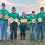 Five people hold plaques while standing near a body of water.