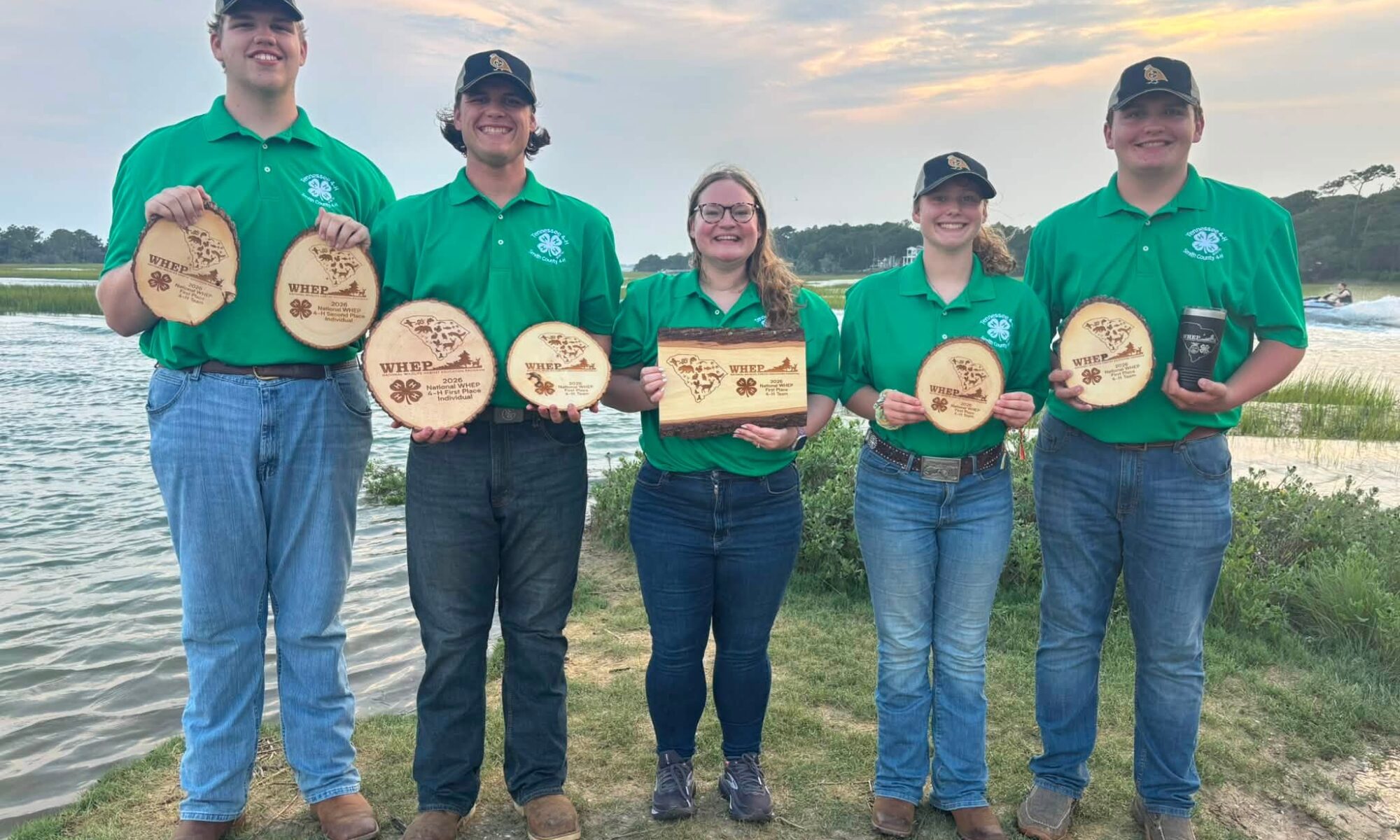 Five people hold plaques while standing near a body of water.