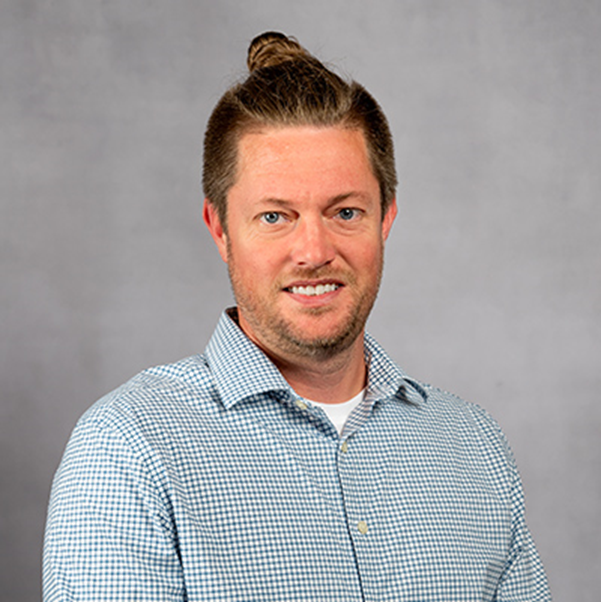 Person in blue button up smiles in front of gray background.