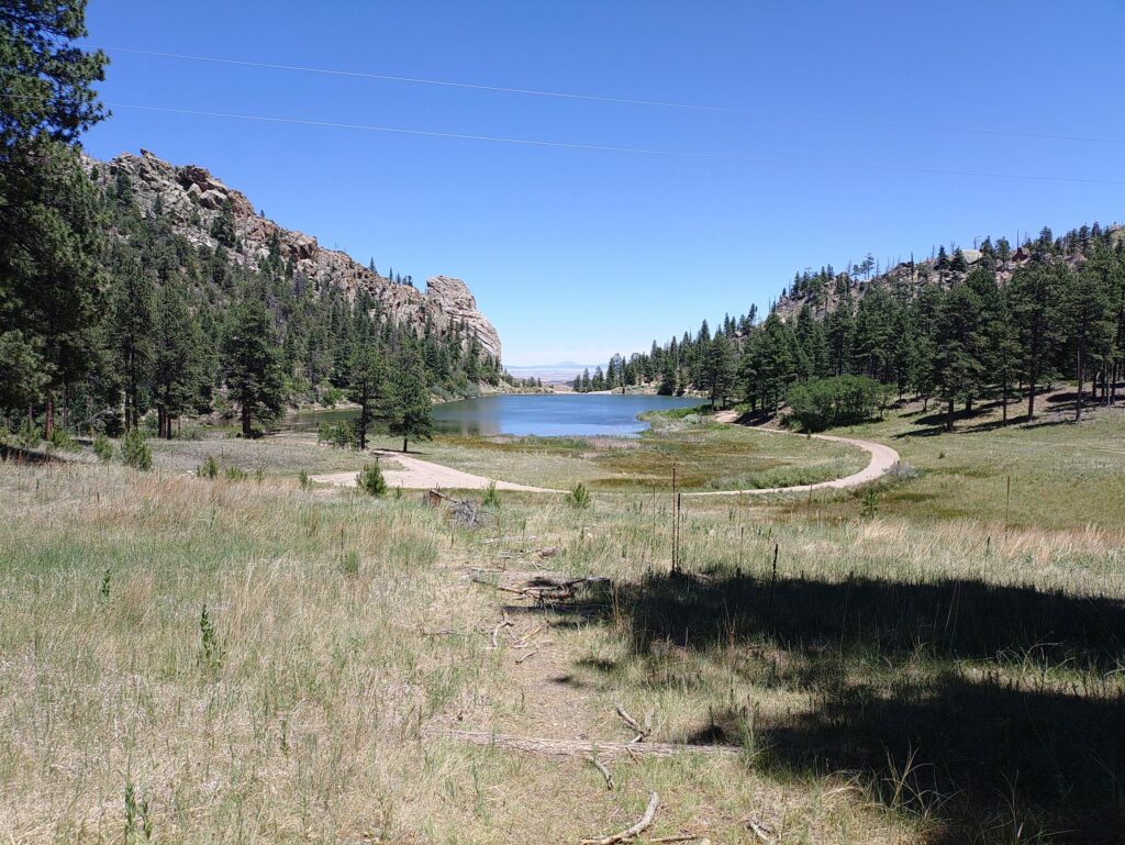 Rocky hills, trees, and grass surround a lake on Philmont Scout Ranch in New Mexico.