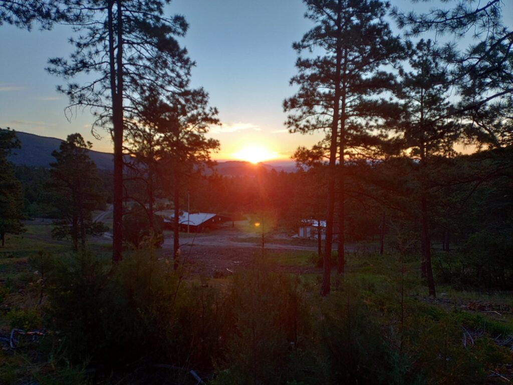 Sun sets over wooded area and building in Philmont Scout Ranch in New Mexico.