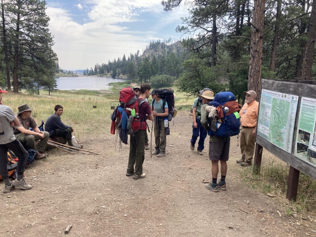 Nine people stand around map of area at Philmont Scout Ranch in New Mexico.