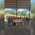 Seventeen people wearing camo stand under an awning to a barn holding an orange banner that says "Tennessee Wildlife Federation."
