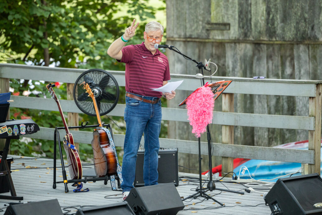 A person wearing a maroon and yellow striped polo speaks into a microphone on Maryville College campus.