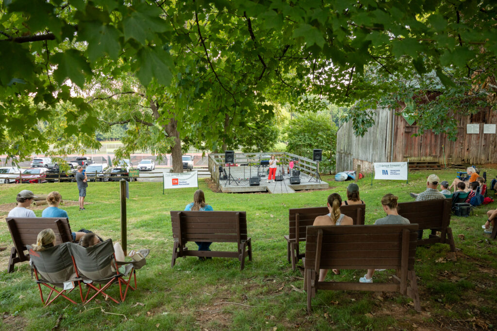 Several people sit on benches listening to a person speak on an outdoor stage on Maryville College campus.