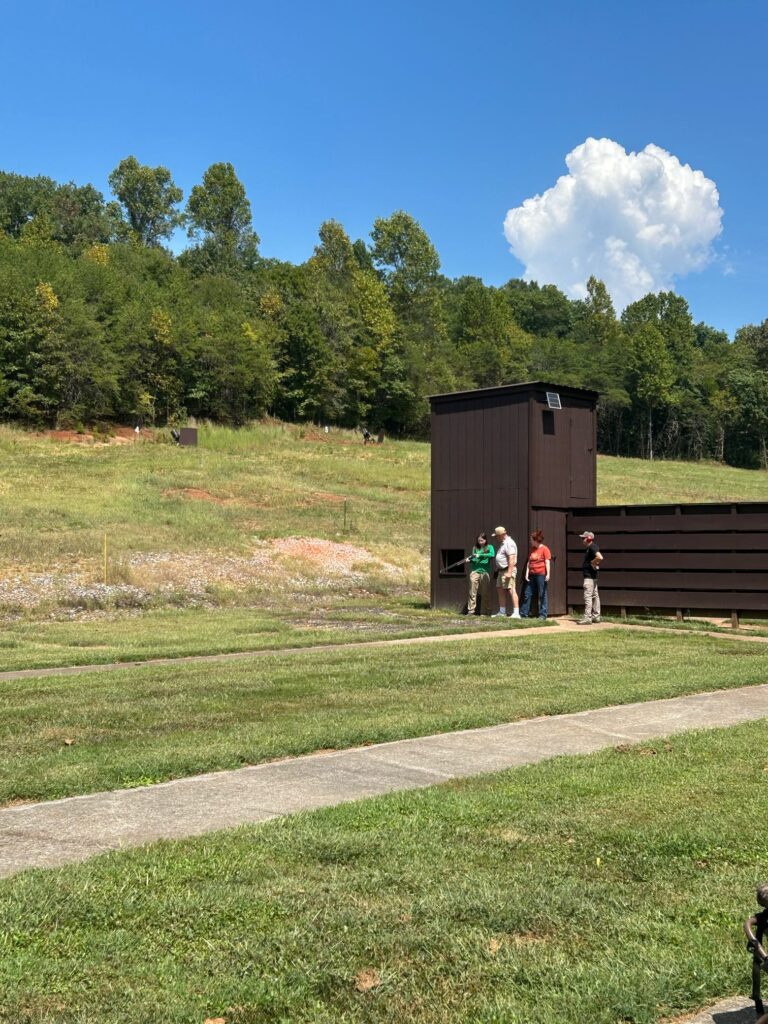 Three people instruct a third on shooting in an empty field.