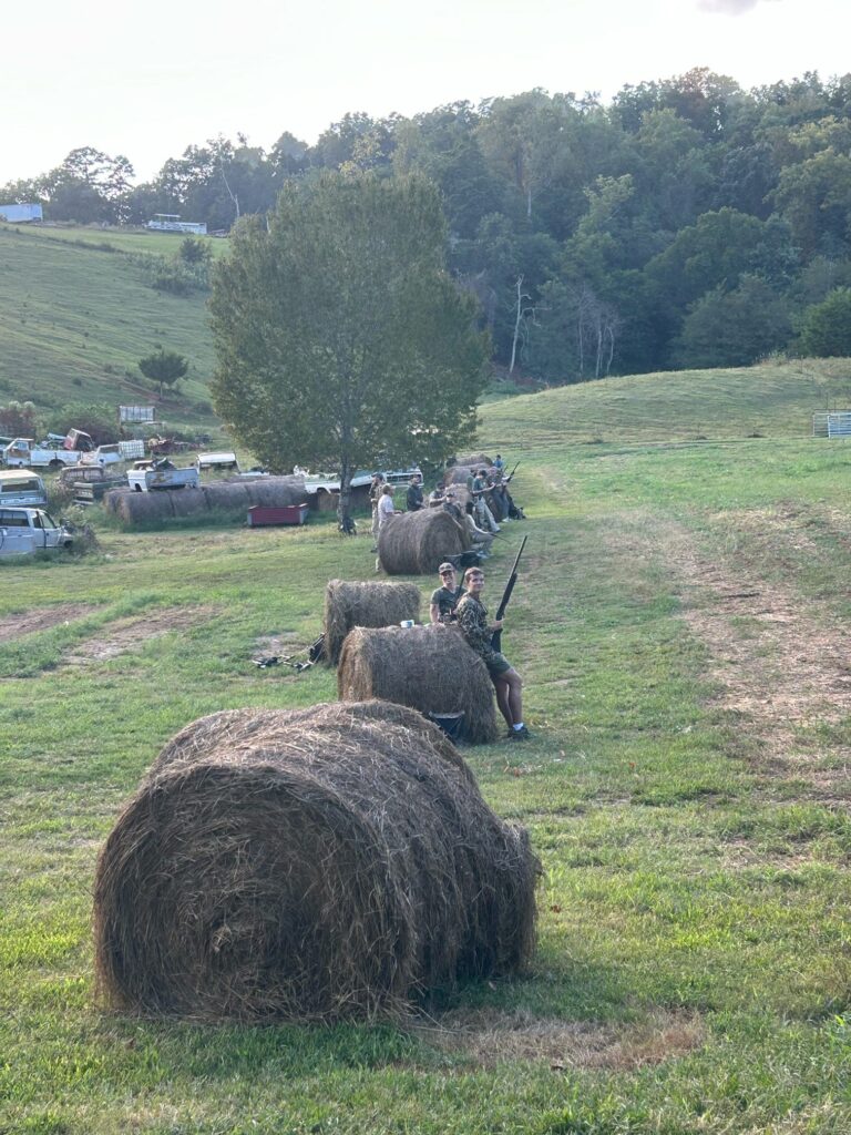 Hunters stand besides hay bales in a field.