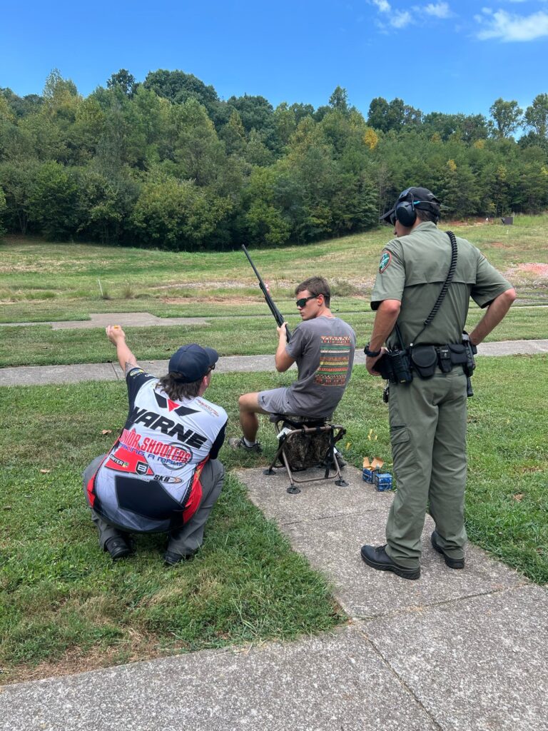 Two people instruct a third on shooting in an empty field.