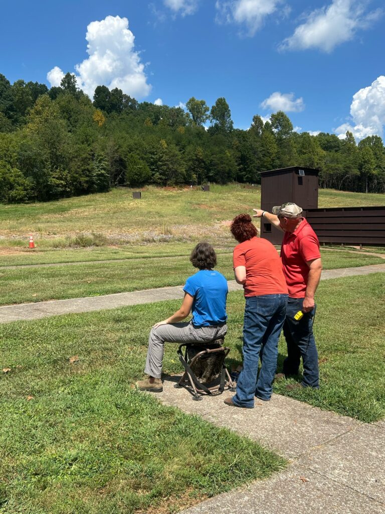 Two people instruct a third on shooting in an empty field.