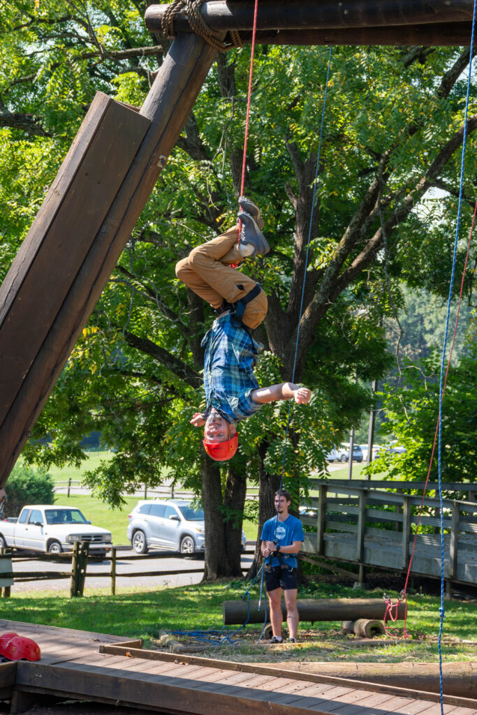 A person hands upside down from a climbing challenge on Maryville College campus.