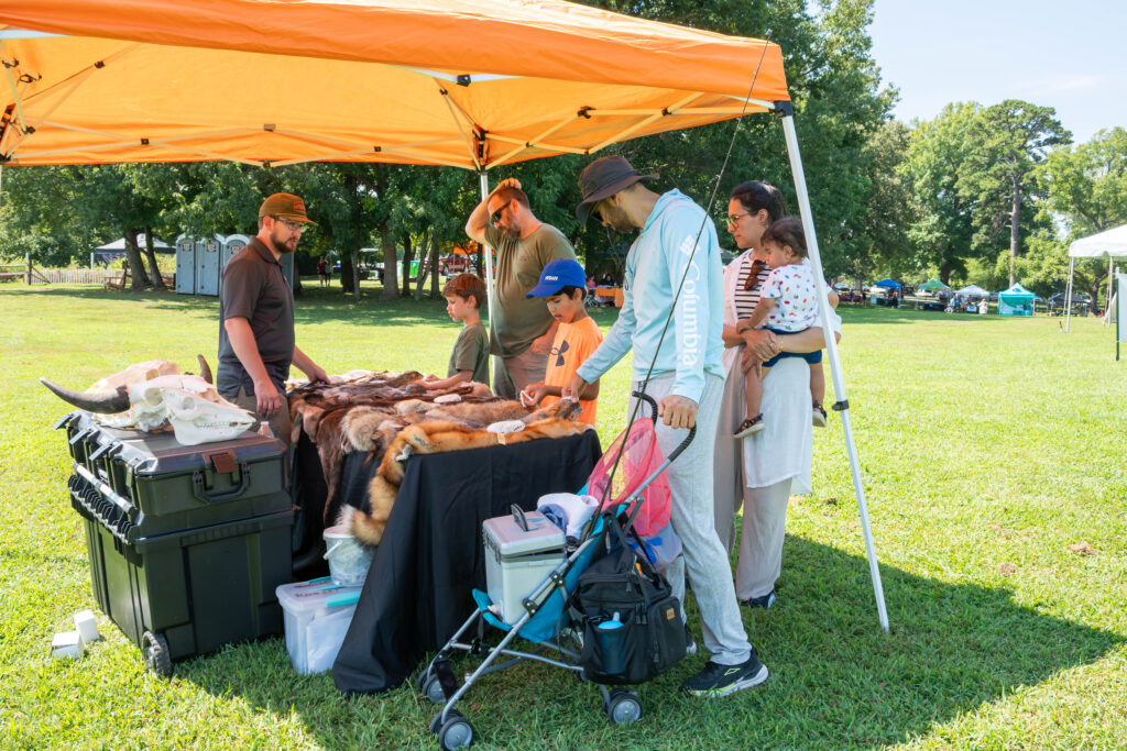 Seven people stand around a table with pelts under a pop up tent on Maryville College campus.