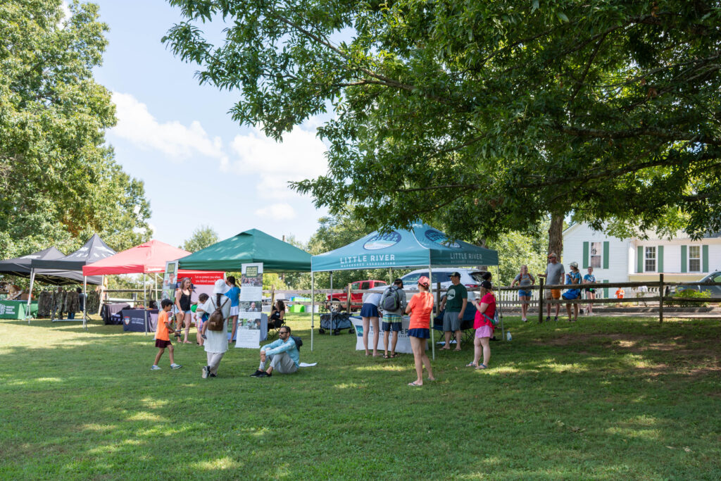 Several people stand or sit by three pop up tents on Maryville College campus.