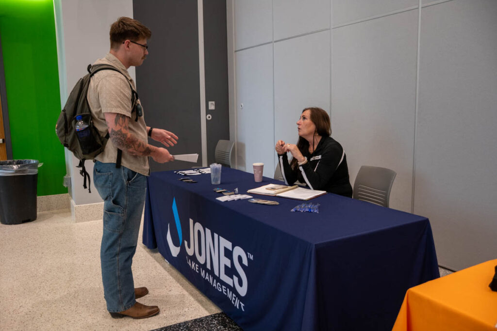 One person sits and another person stands at a table in a building on the UT Institute of Agriculture campus.