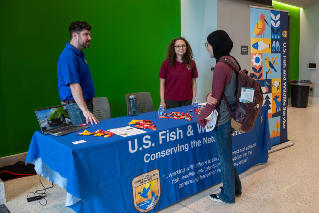 Three people stand and talk around a table with a tablecloth saying "U.S. Fish and Wildlife" in a building on the UT Institute of Agriculture campus.