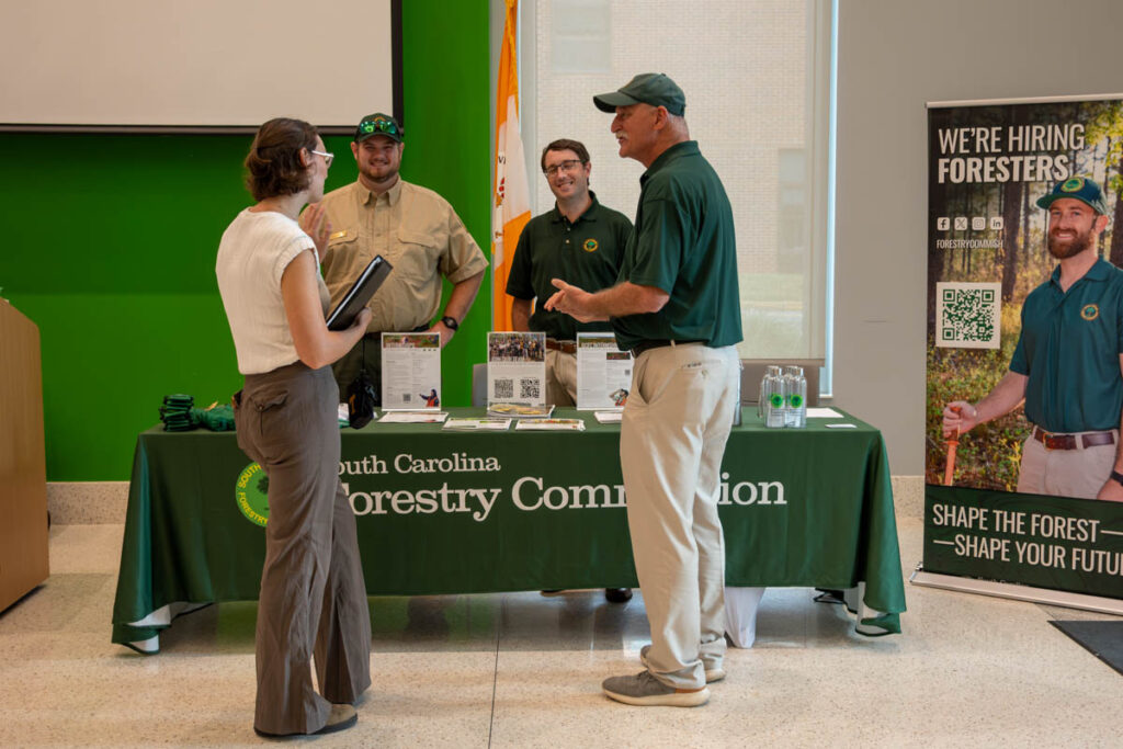 Four people stand and talk around a table with a green tablecloth in a building on the UT Institute of Agriculture campus.