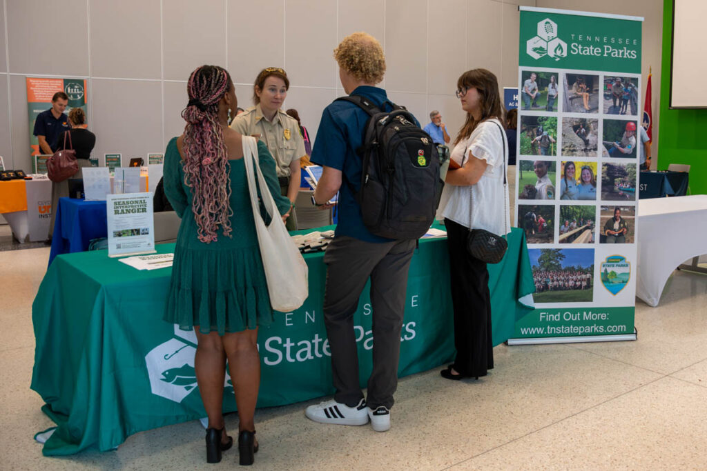 Four people stand and talk around a table with a green tablecloth in a building on the UT Institute of Agriculture campus.