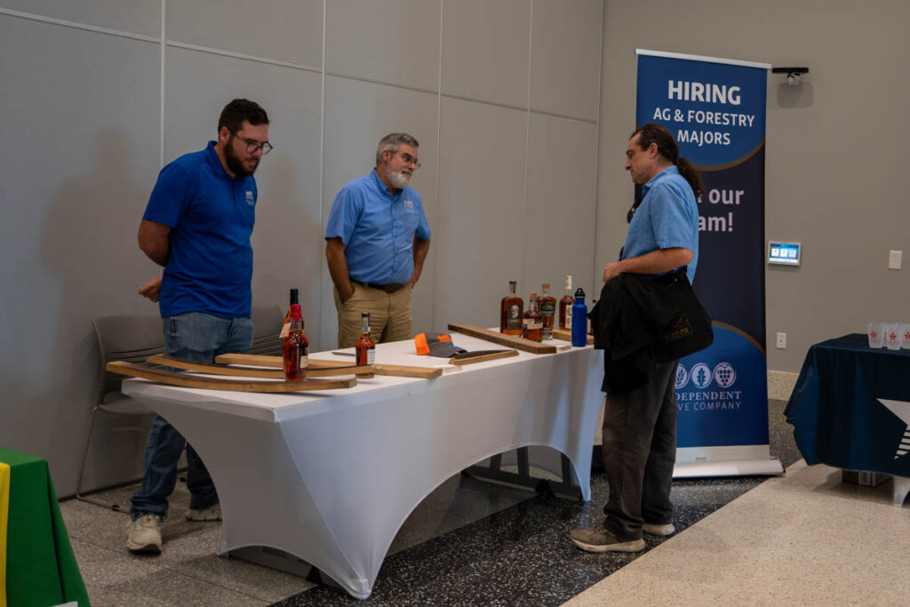 Three people stand around a table with a white tablecloth and wood on it in a building on the UT Institute of Agriculture campus.