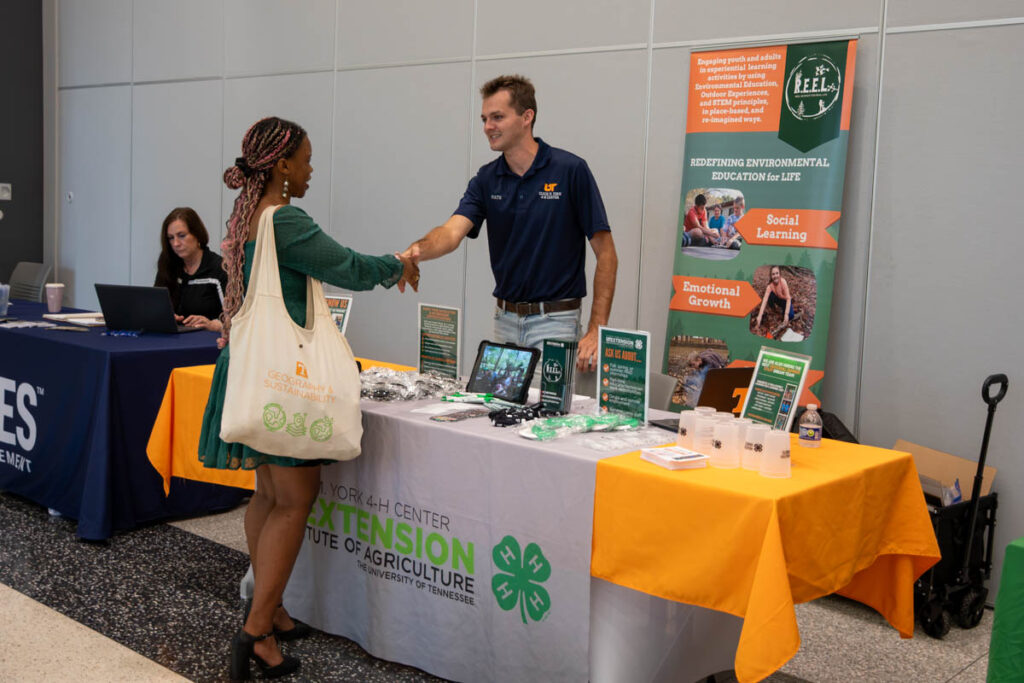 Two people shake hands at a table in a building on the UT Institute of Agriculture campus.
