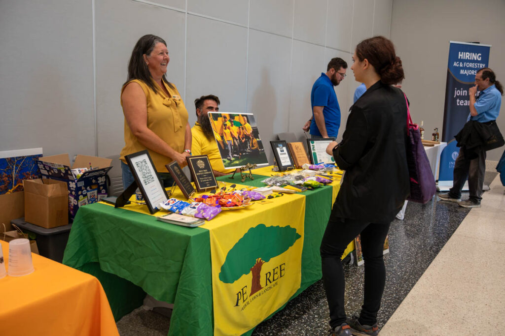 Two people stand and another sits at a table with a yellow and green tablecloth in a building on the UT Institute of Agriculture campus.