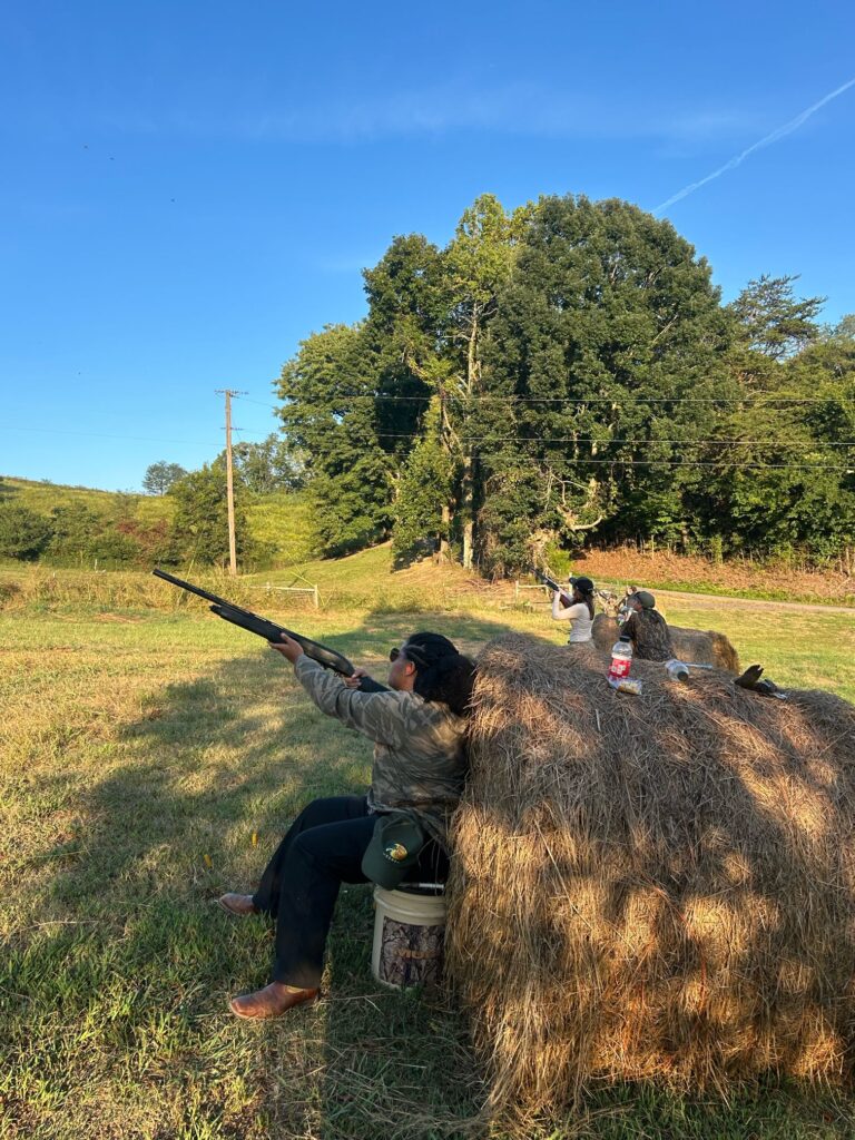 One person shoots a gun into the air next to a hay bale.