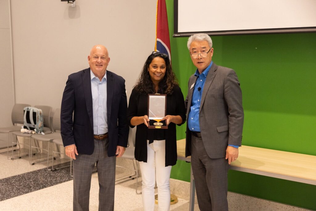 Three people stand in the Agriculture and Natural Resources Building on the UT Institute of Agriculture with the middle person holding a medal.