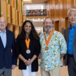 Four people stand in the Agriculture and Natural Resources Building, on the UT Institute of Agriculture campus with two of them wearing medals.