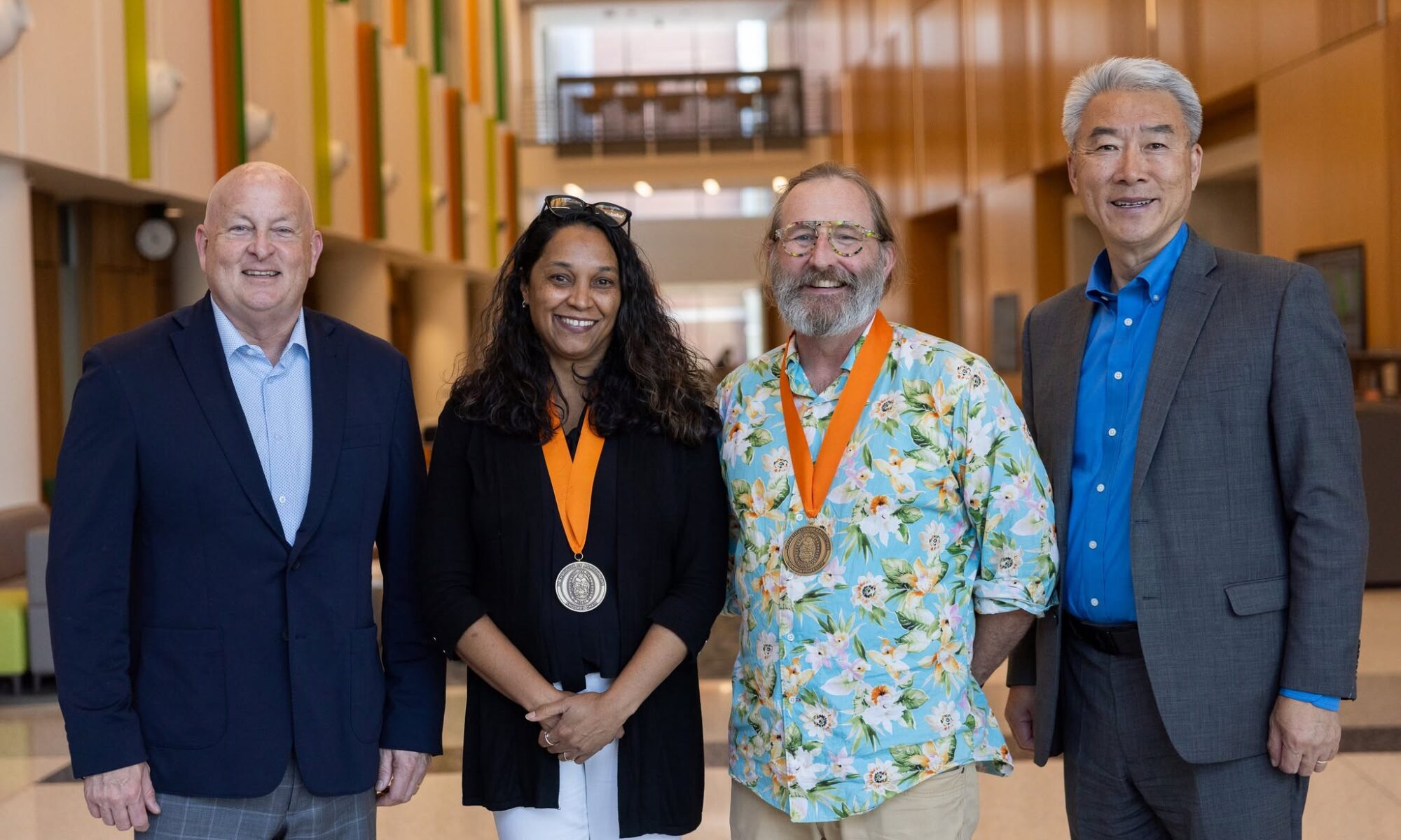 Four people stand in the Agriculture and Natural Resources Building, on the UT Institute of Agriculture campus with two of them wearing medals.
