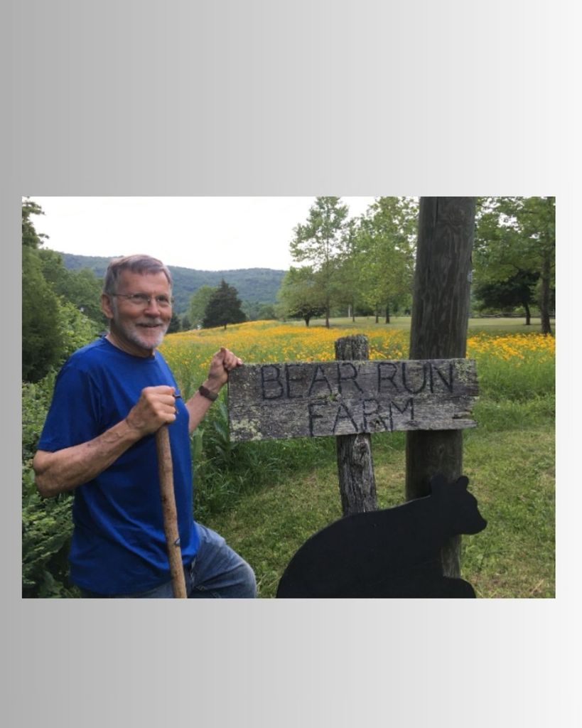 Man holding stick stands next to sign that says bear run farm.