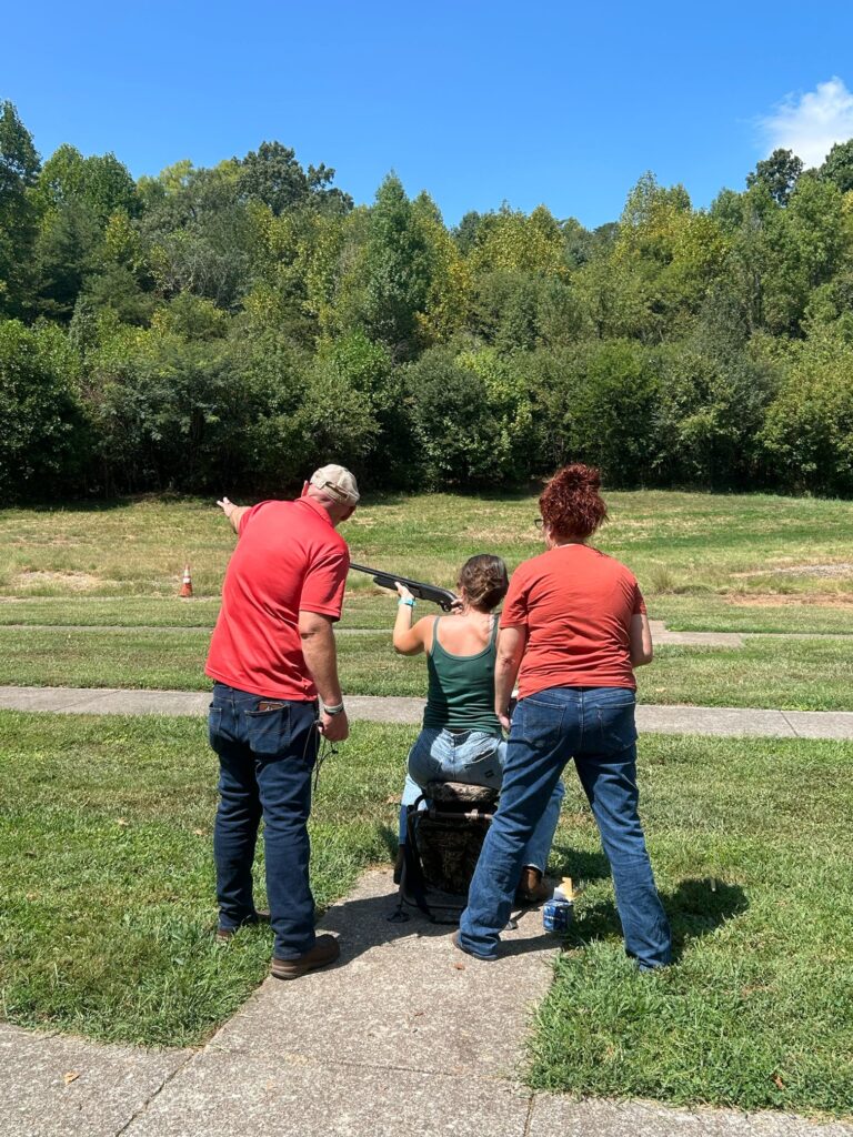 Two people instruct a third person shooting a gun.