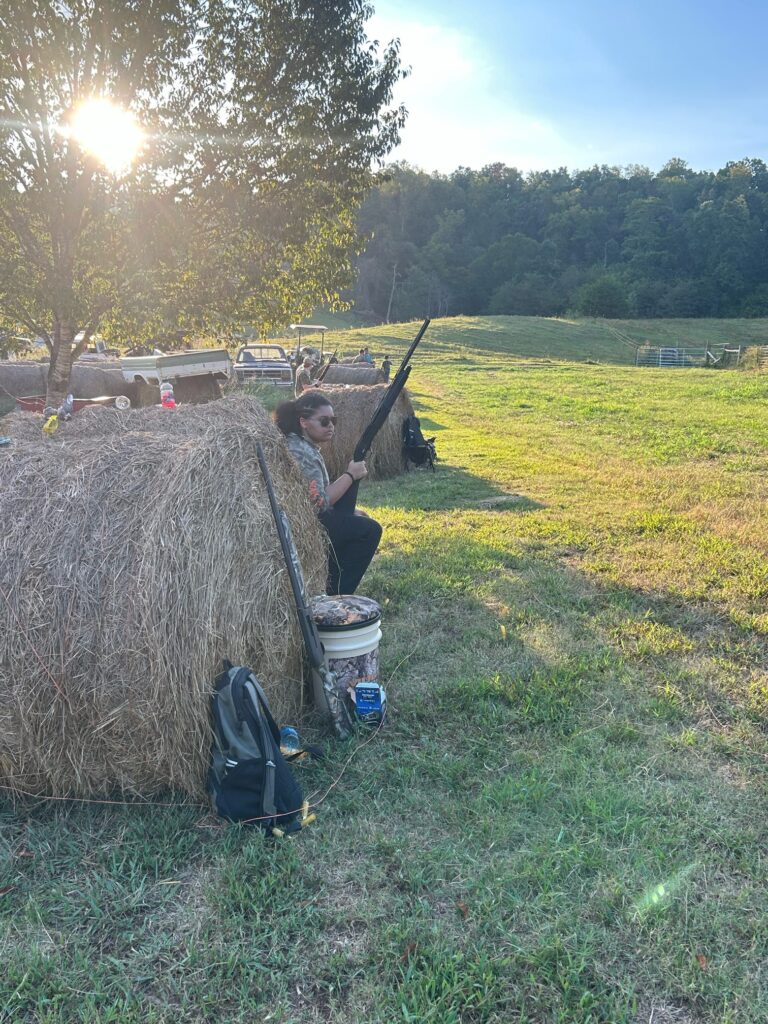 One person holds a gun by a hay bale.