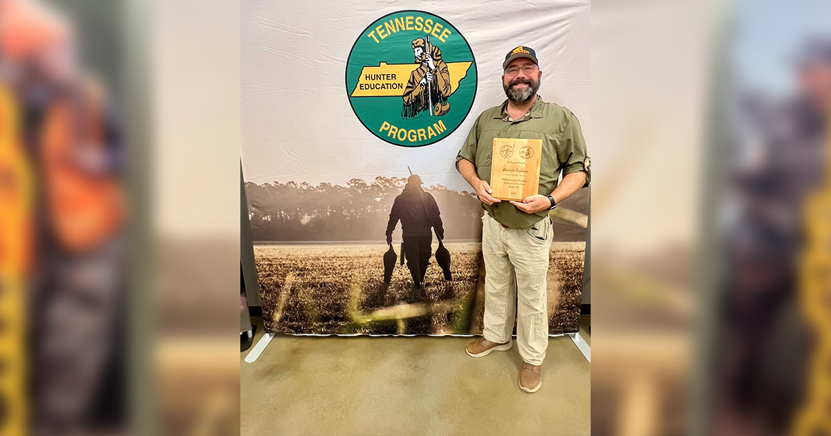 Man stands in front of banner for Tennessee Volunteer Educator Program holding wooden plaque.