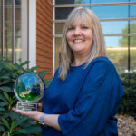 Person wearing blue shirt holds a green and blue glass award outside a building on the UT Institute of Agriculture campus.